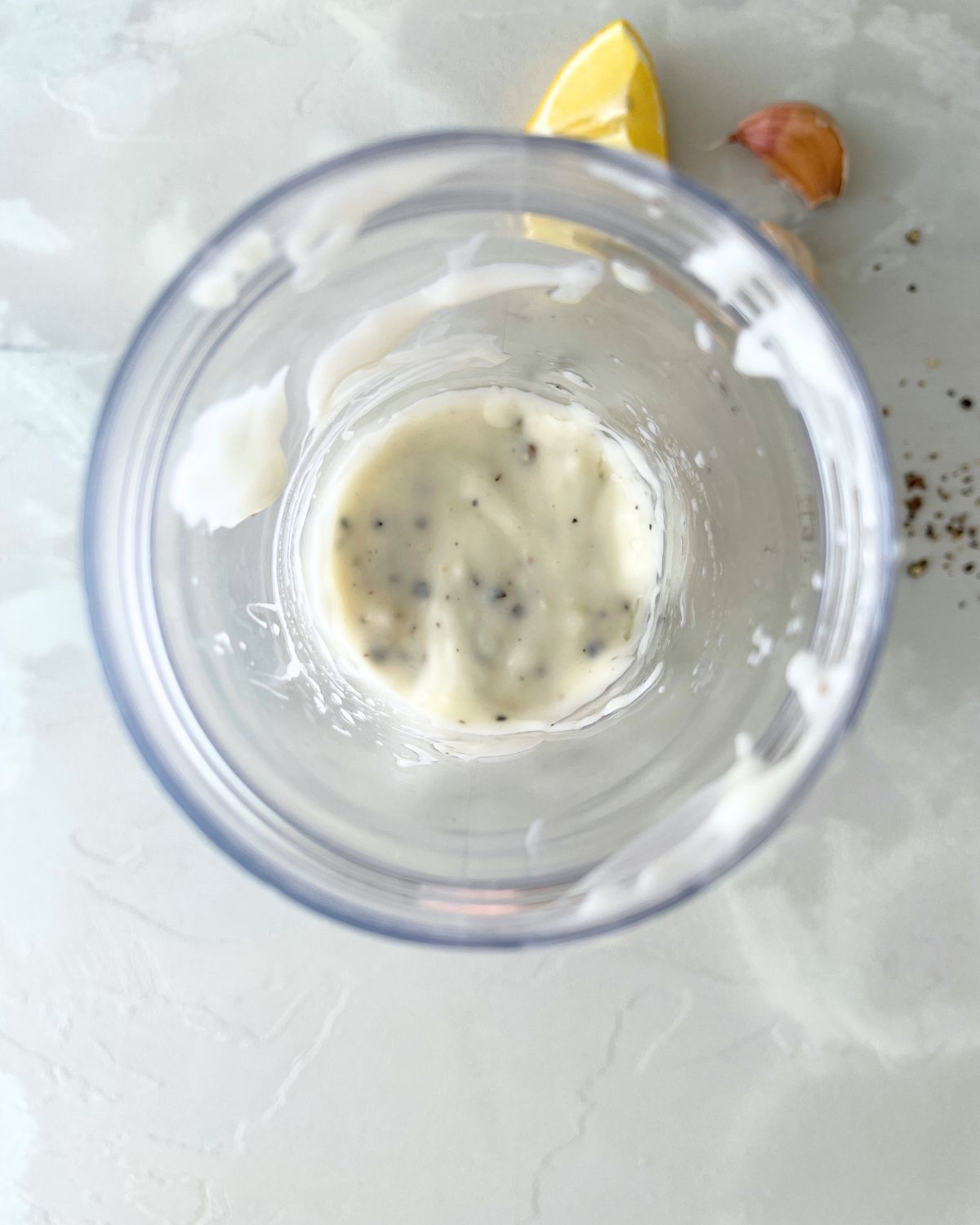 Freshly blended black pepper aioli in a food processor bowl showing the smooth, creamy, pale yellow sauce with visible black pepper specks throughout.