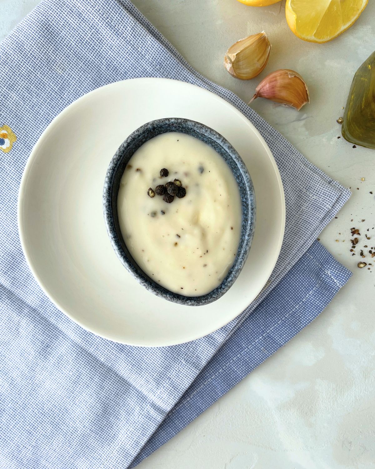 A white bowl filled with creamy black pepper aioli, showing the speckled pepper throughout the pale yellow sauce, with a spoon resting in the bowl.