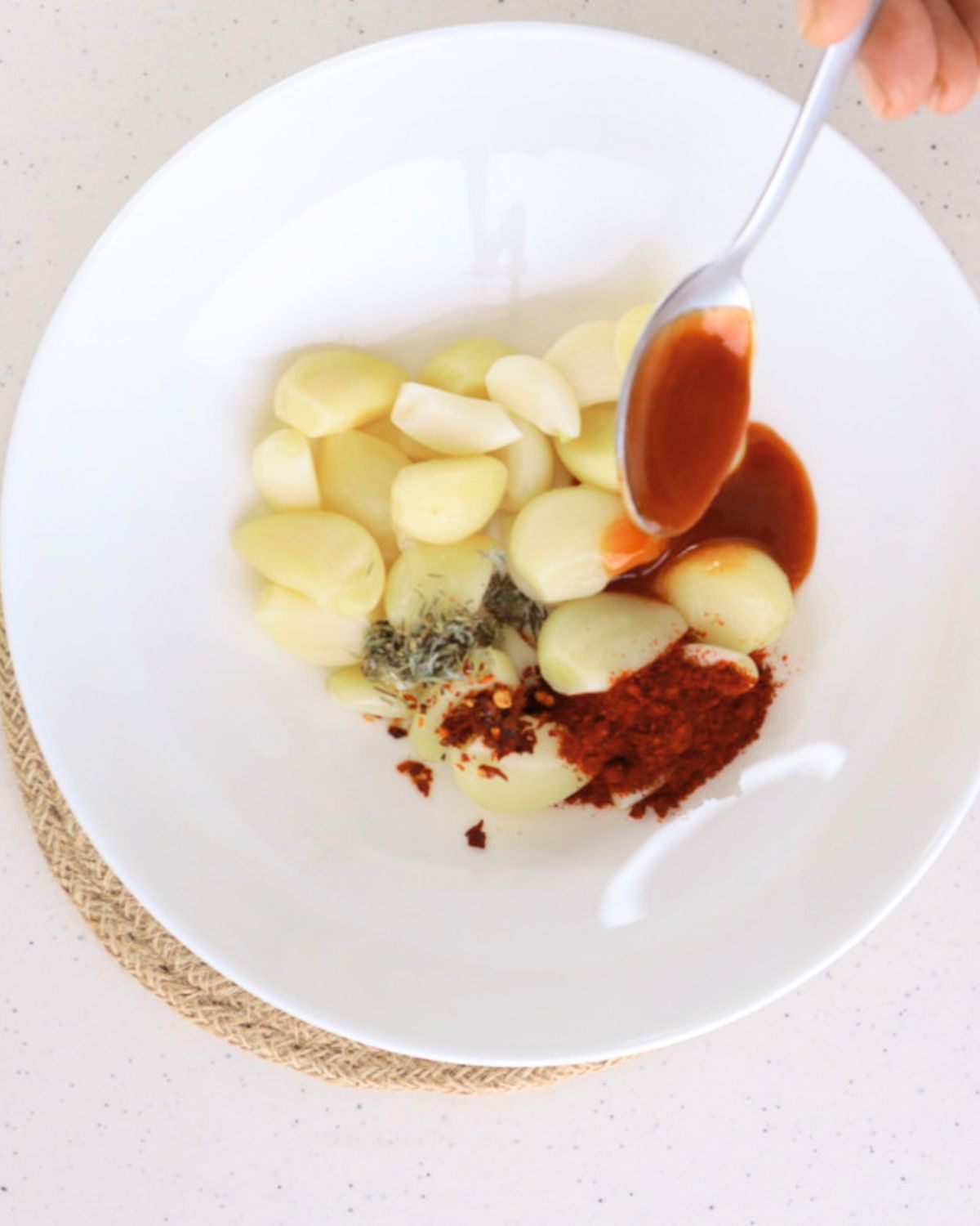 Peeled fresh garlic cloves combined in a bowl with dried thyme, cayenne, Sriracha sauce, and red chili flakes, being mixed together to coat the garlic for TikTok spicy pickled garlic.
