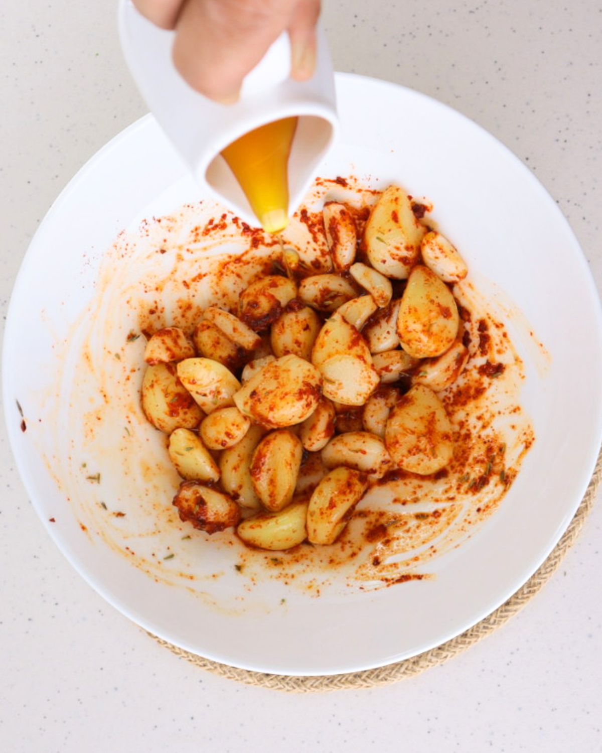 Honey being drizzled over the Sriracha and spice-coated garlic cloves in a bowl before the final mix for TikTok spicy pickled garlic.
