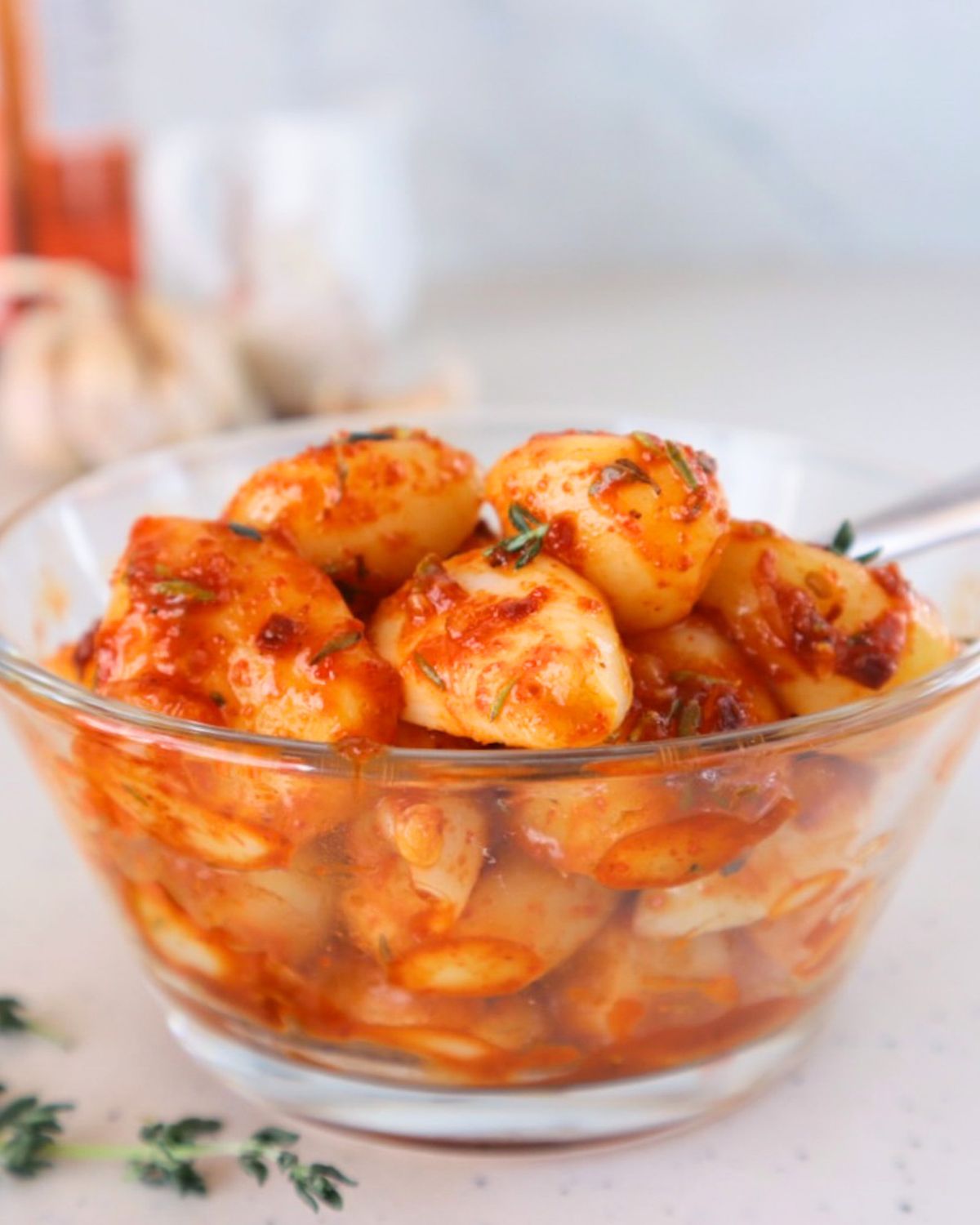 Finished TikTok spicy pickled garlic in a glass bowl showing whole garlic cloves evenly coated in glossy red Sriracha and honey mixture with visible chili flakes.