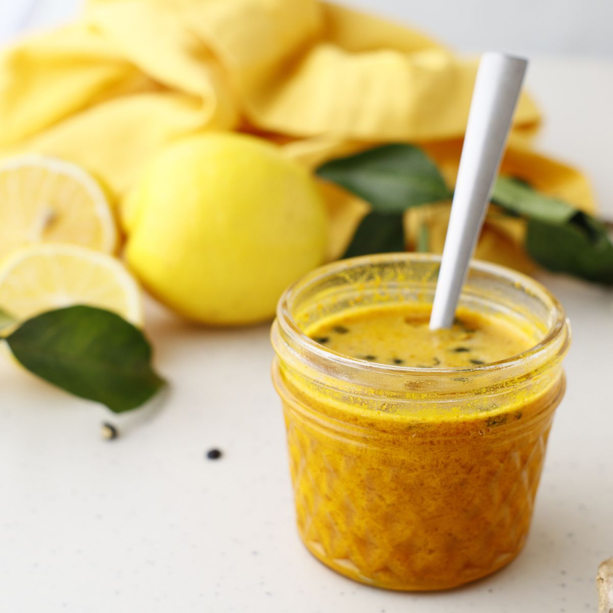 Side view image of Turmeric Ginger Honey with spoon in a jar with lemon in the background