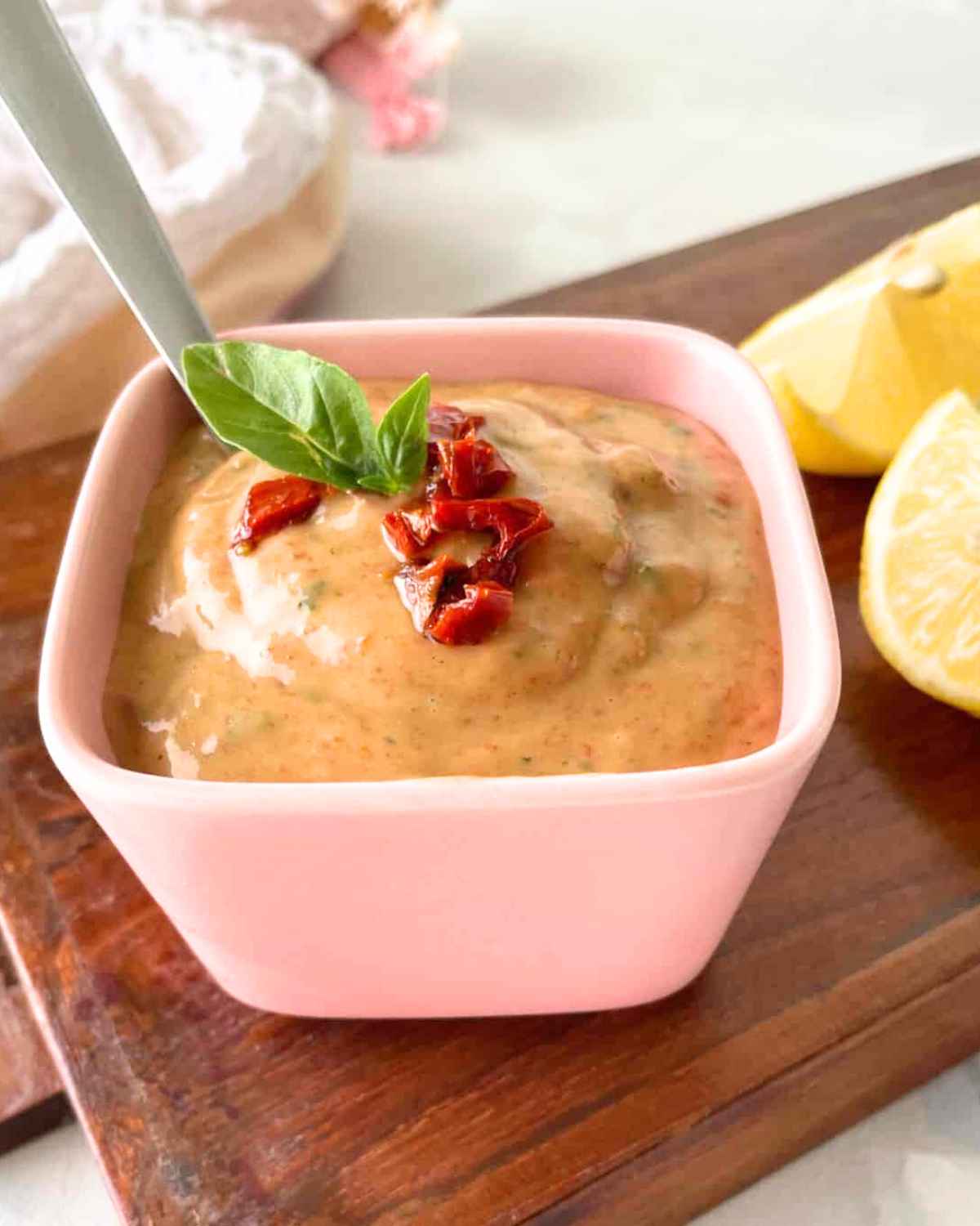 Side top view image of Sun Dried Tomato Aioli garnished with sundried pieces and mint leaves with spoon in a bowl