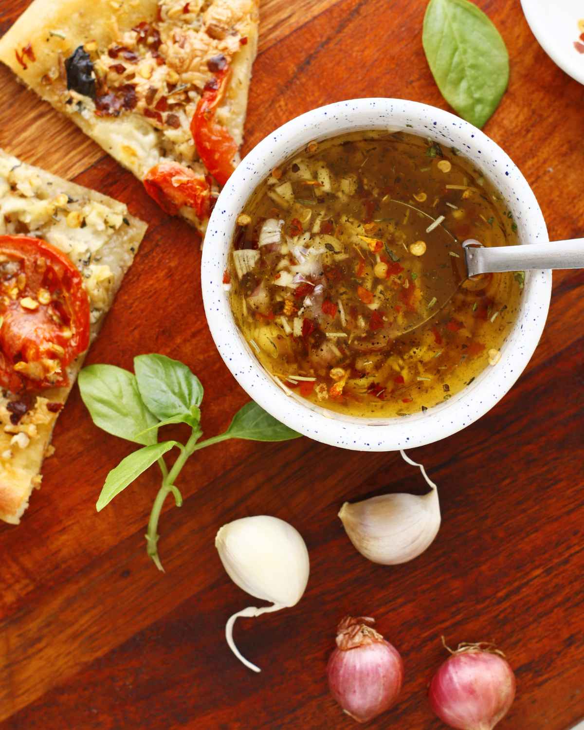 Delicious Olive Oil Pizza Sauce with spoon in bowl and some pizza slices in the background