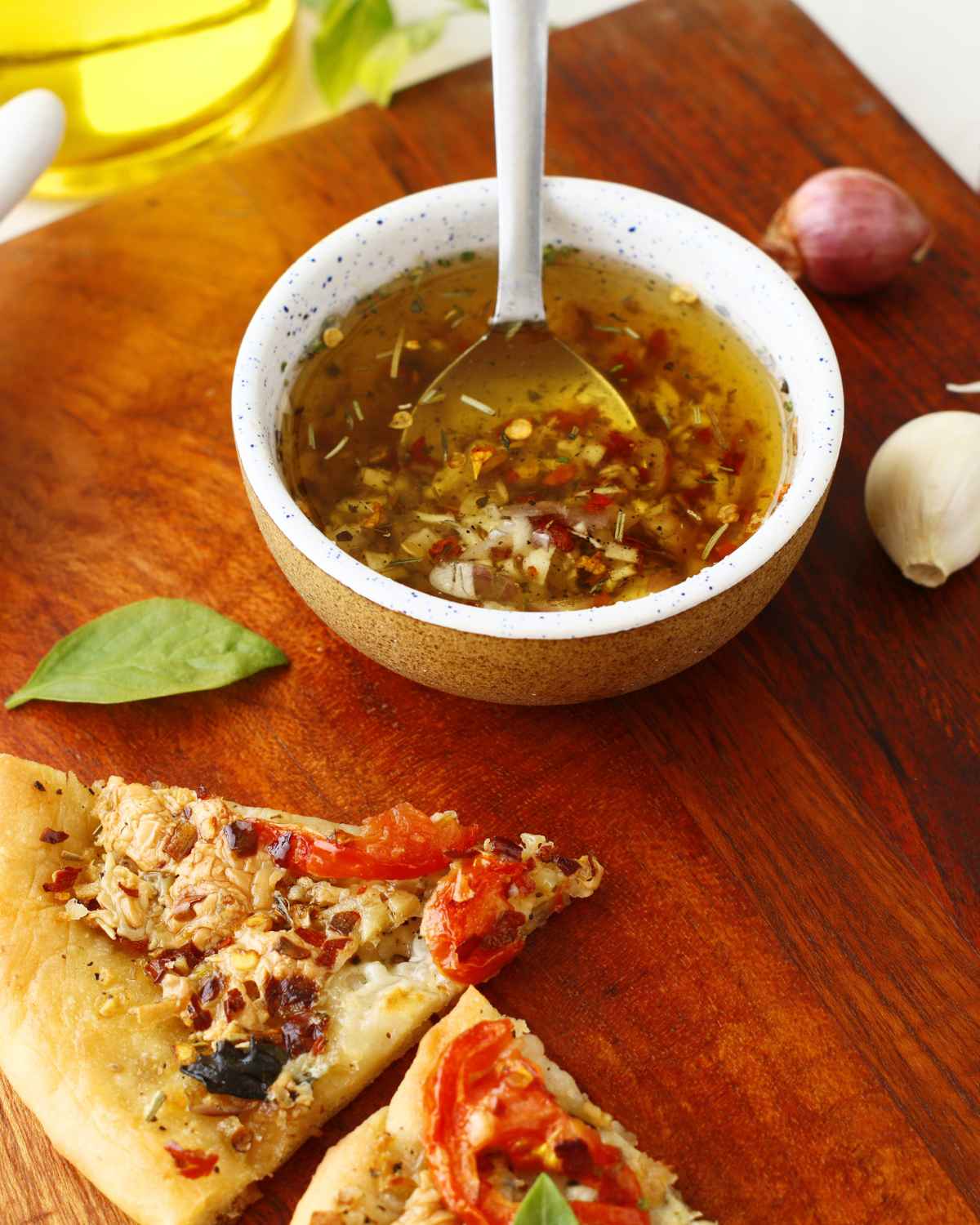 Top side view image of Olive Oil Pizza Sauce in bowl and some pizza slices in the background