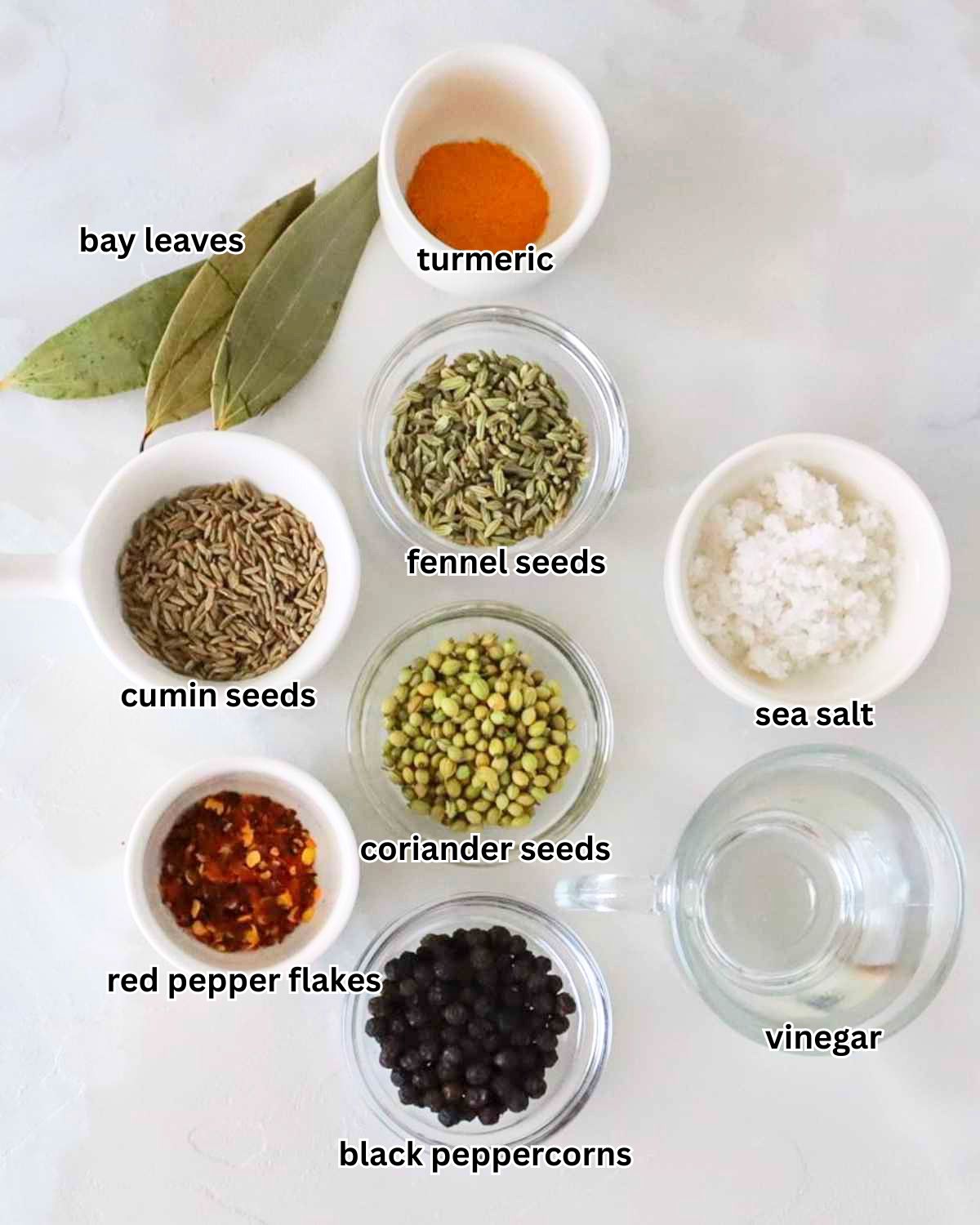 Supporting spice ingredients for Persian Torshi Makhloot including whole black peppercorns, cumin seeds, fennel seeds, coriander seeds, red pepper flakes, bay leaves, and a small bowl of ground turmeric on a white surface.