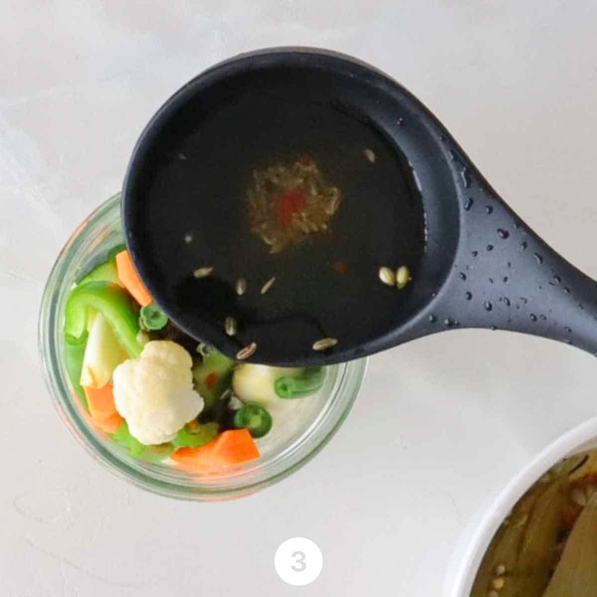 Mixed vegetables — cauliflower, cucumber, carrot, celery, bell pepper, green beans, and whole garlic cloves — packed tightly into clean glass jars ready for the hot pickling brine.
