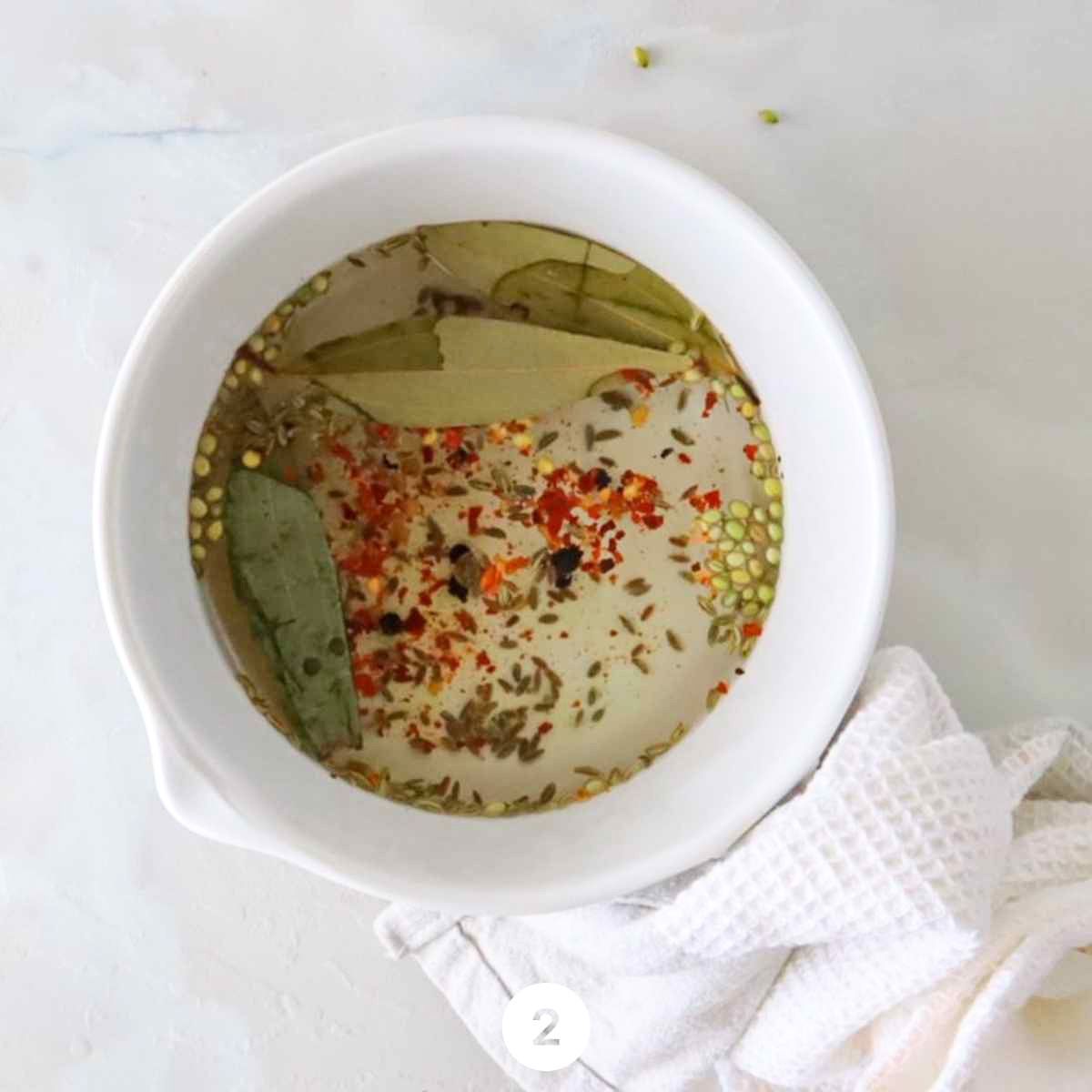 White vinegar, water, sea salt, turmeric, black peppercorns, cumin seeds, fennel seeds, coriander seeds, bay leaves, and red pepper flakes combined in a large pot on medium heat, being brought to a boil to make the Torshi pickling brine.